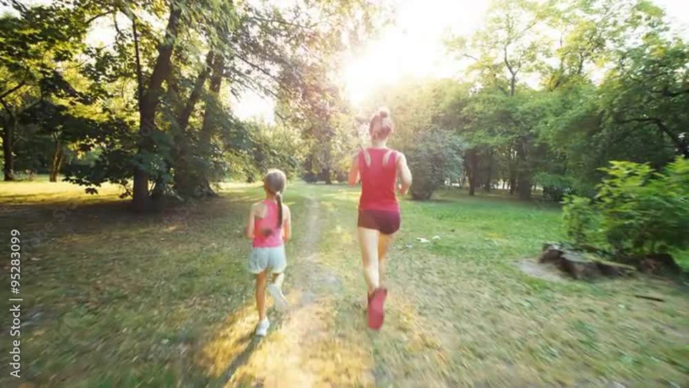 Athletes family mother and daughter running away from camera in the park in sunlight. Lens flare Athletes family mother and daughter running away from camera in the park in sunlight. Lens flare