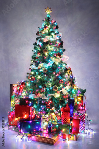 Decorated Christmas tree with colorful lights surrounded by pres