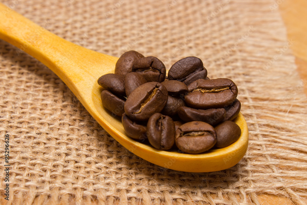 Obraz premium Heap of coffee beans with wooden spoon on jute canvas