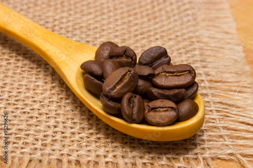 Heap of coffee beans with wooden spoon on jute canvas