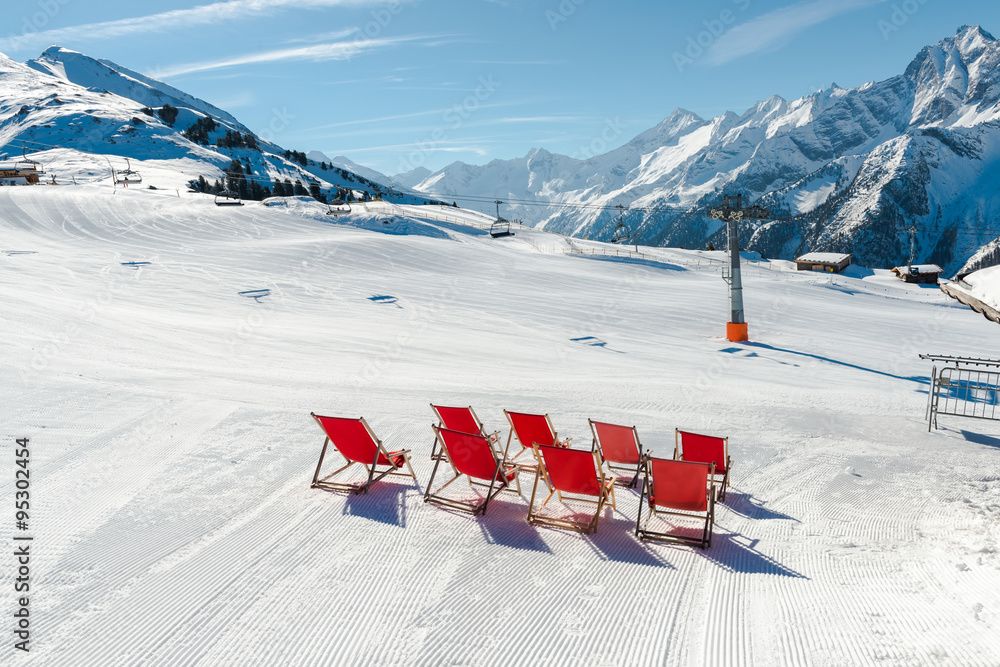 Naklejka premium Empty red deck chairs on the snow in a ski resort, Austrian Alps