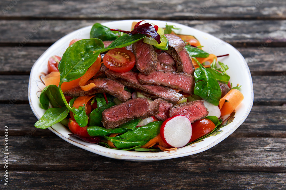 Spicy Beef Slices Meat Salad with Carrots, Tomatoes, Cucumber, Parsley and Salad leaves Spinach, rocket, red ruby chard on old wooden table