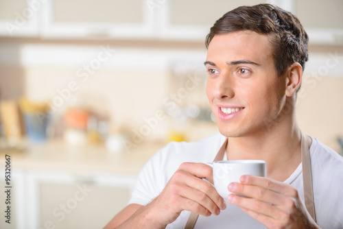 Smiling young man enjoys a cup pf coffee.