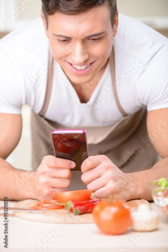 Young attractive cook using his smartphone.