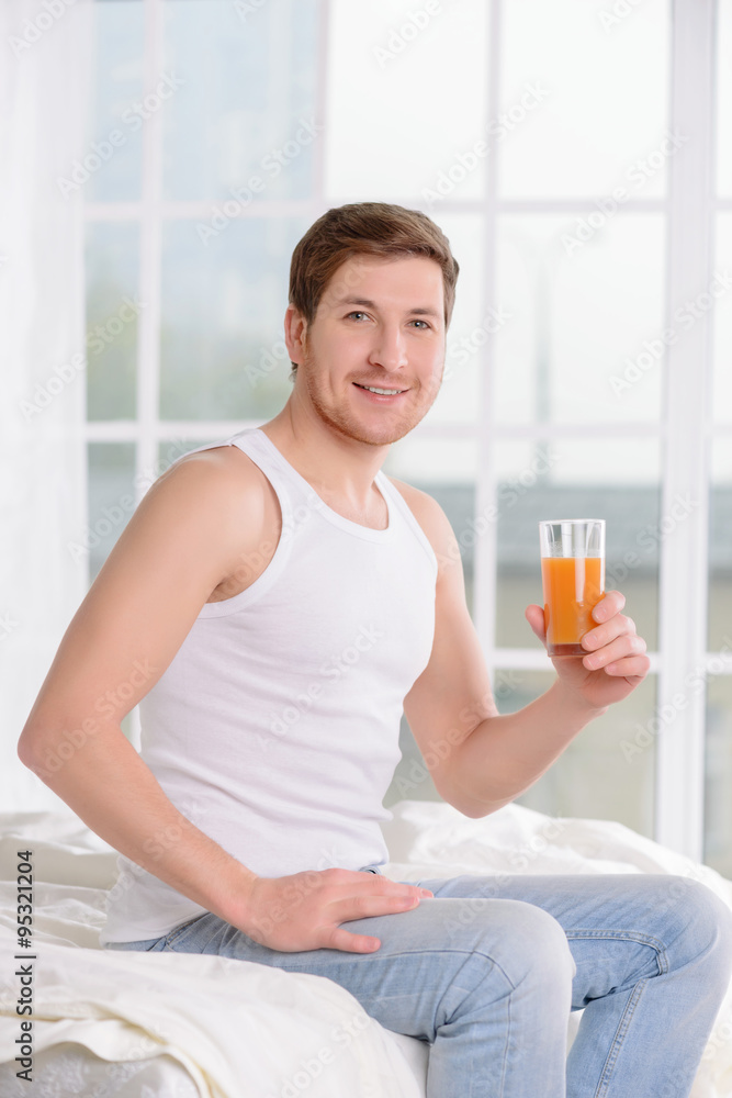 Young man sitting on bed with glass of juice. Young man sitting on bed with glass of juice.