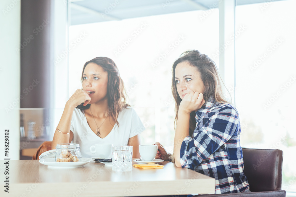 Two young and beautiful women meet at the bar for a cappuccino and to chat .Both observe the inside of the bar