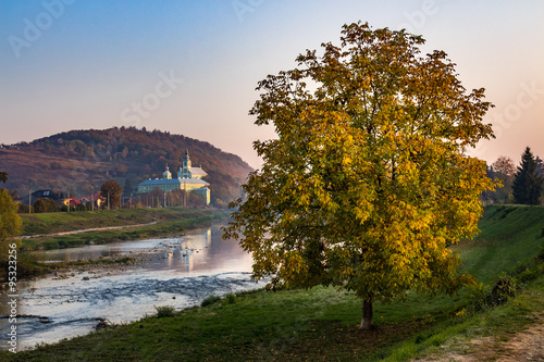 Monasteryon a hill  and tree near river in hazy autumn sunrise photo