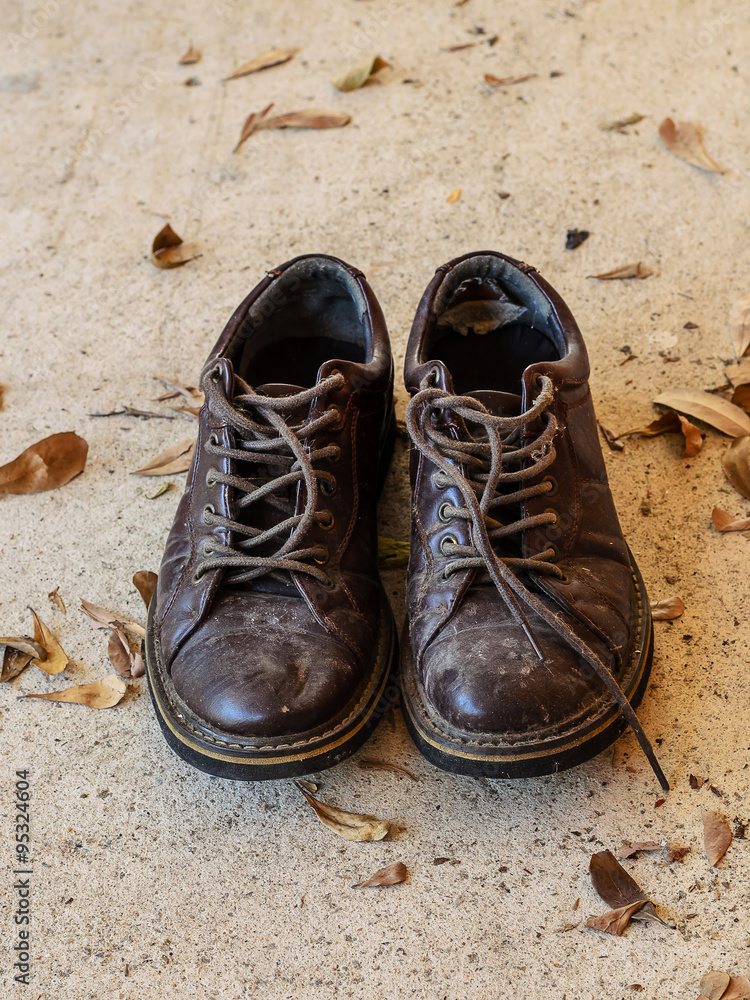 Naklejka premium Old and dirty men brown leather shoes with dry leaves on concret