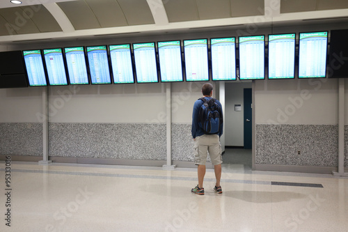 Man is looking and pointing at a departure/arrival board at an airport
