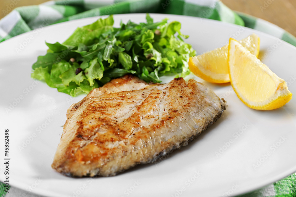 Dish of fish fillet with greens and lemon on plate close up Dish of fish fillet with greens and lemon on plate close up
