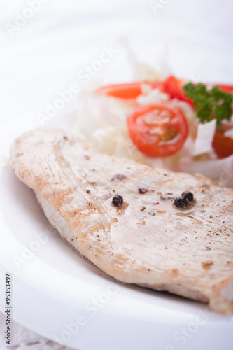 Roasted chicken filet with vegetables on a white plate. Closeup
