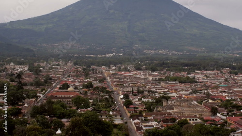 Establishing wide view of the old city of Antigua in Guatemala with camera tilt up to the Pacaya volcano revealing volcanic plume smoke, sky, and clouds surrounding the ancient Mayan city. photo