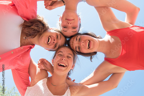 Under view of four trendy girlfriends arm in arm. 