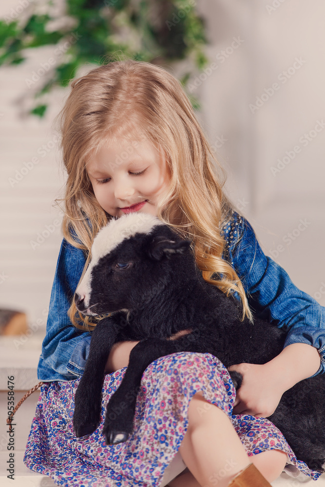 Little girl playing with a baby goat on a house porch Little girl playing with a baby goat on a house porch
