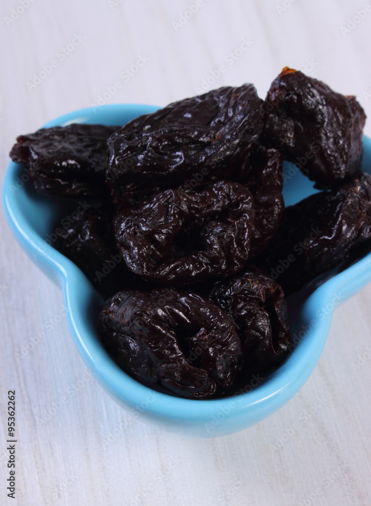 Dried plums in blue bowl on wooden table, healthy food Dried plums in blue bowl on wooden table, healthy food