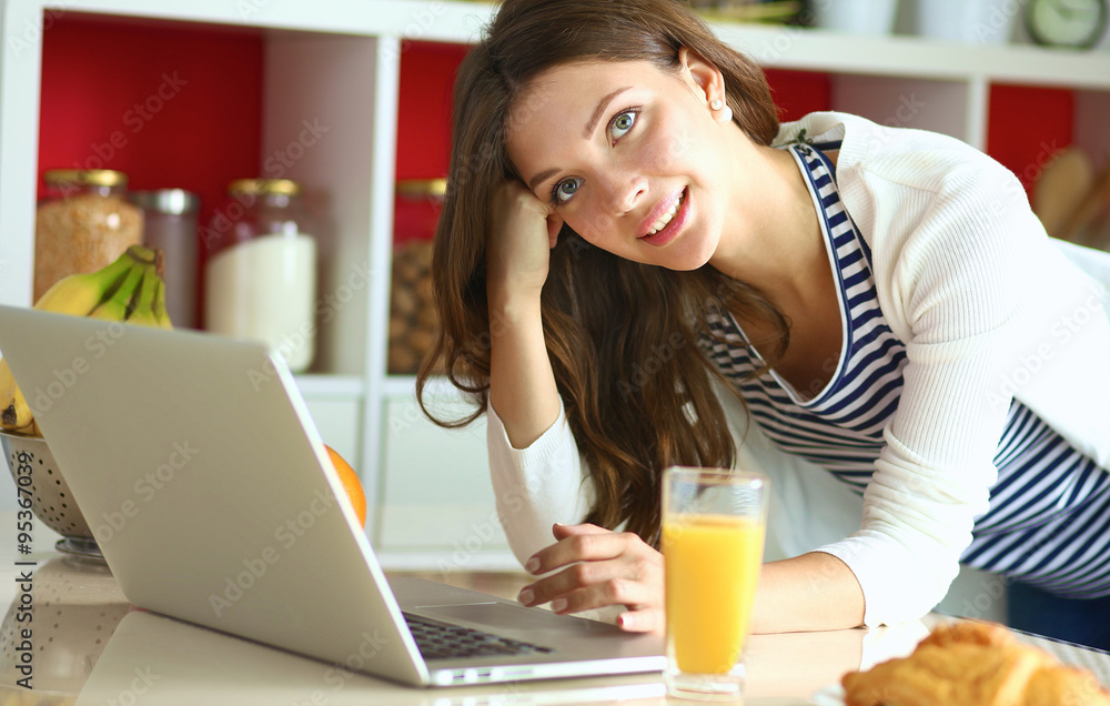 Attractive young woman using laptop and sitting in the kitchen Attractive young woman using laptop and sitting in the kitchen