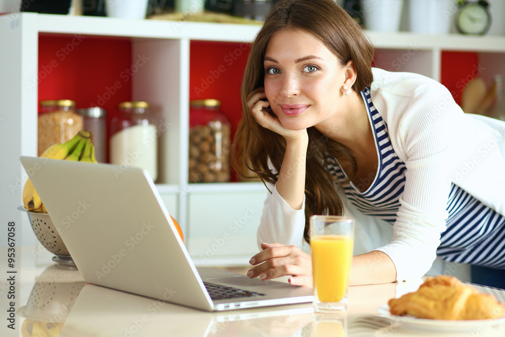 Attractive young woman using laptop and sitting in the kitchen Attractive young woman using laptop and sitting in the kitchen