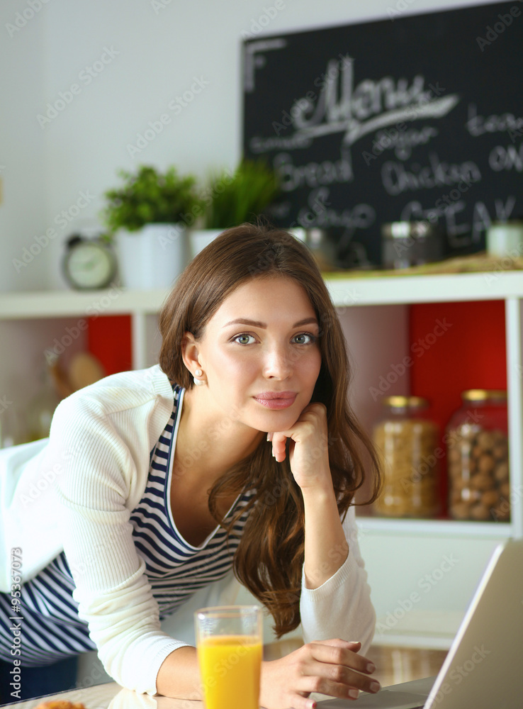 Attractive young woman using laptop and sitting in the kitchen Attractive young woman using laptop and sitting in the kitchen