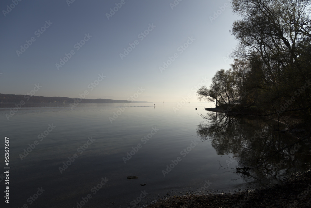 A lake with some boats and a paddler in the autumn morning