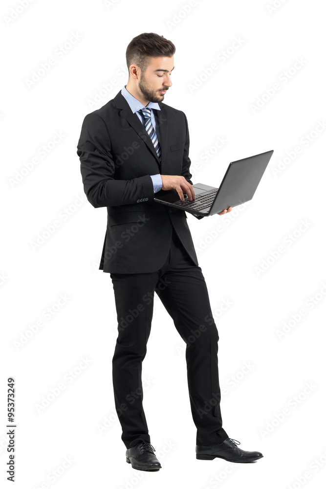 Side view of young businessman in suit using laptop.  Full body length portrait isolated over white studio background. 