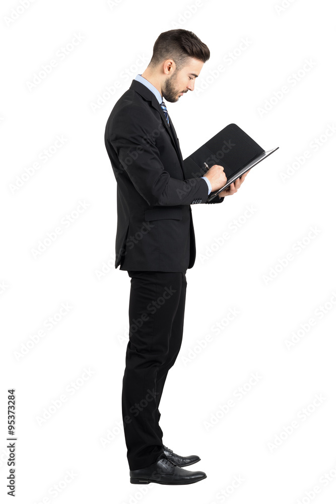 Side view of young businessman in suit signing contract. Full body length portrait isolated over white studio background. 
