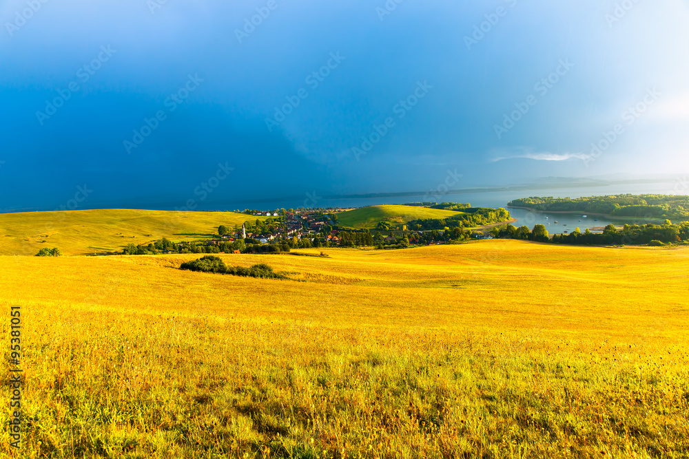 Beautiful landscape, green and yellow meadow and lake with village. Slovakia, Central Europe.