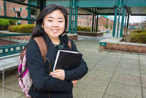 Fotografie Smiling Female Student on Campus with Book and Backpack