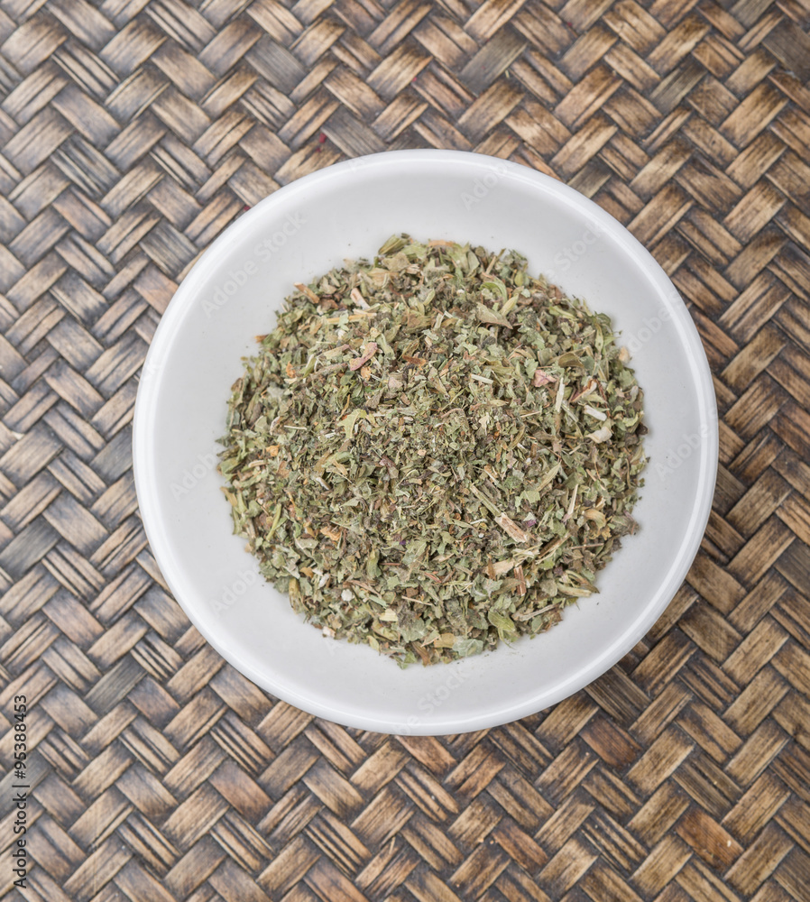 Dried lemon balm leaves in white bowl over wicker background Dried lemon balm leaves in white bowl over wicker background