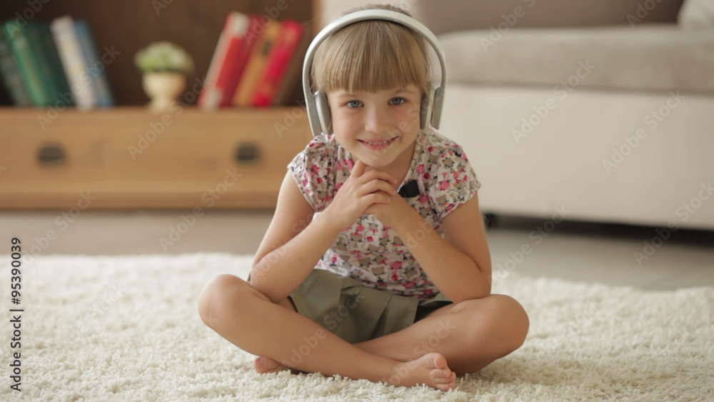 Beautiful little girl in headphones sitting on floor and smiling at camera Beautiful little girl in headphones sitting on floor and smiling at camera