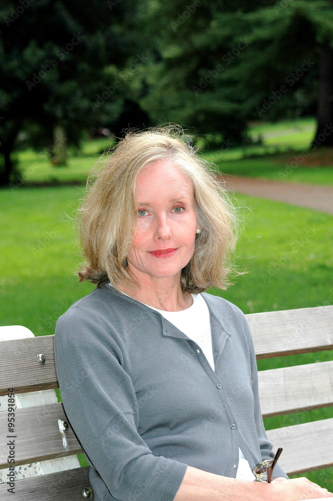 Mature female blond beauty relaxing on a park bench outside. Mature female blond beauty relaxing on a park bench outside.