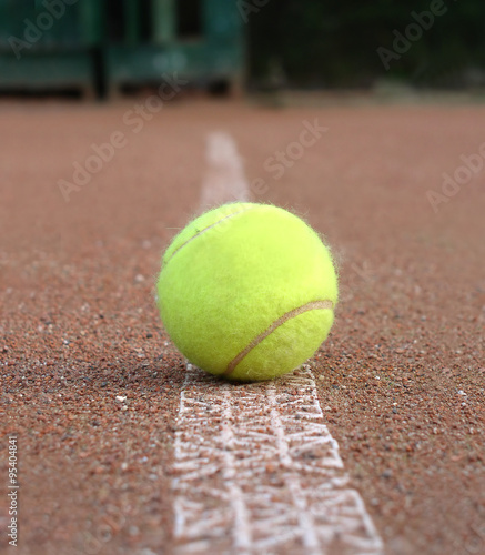 Front view of yellow tennis ball lays on ground outdoor court marking line closeup