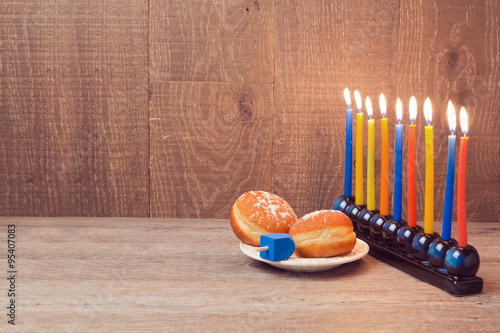 Hanukkah menorah with colorful candles and sufganioyt over wooden background photo