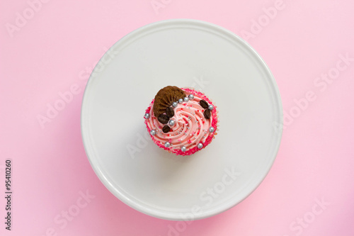 Pink decorated cupcake on white cake stand and pink background, top view, minimal style.