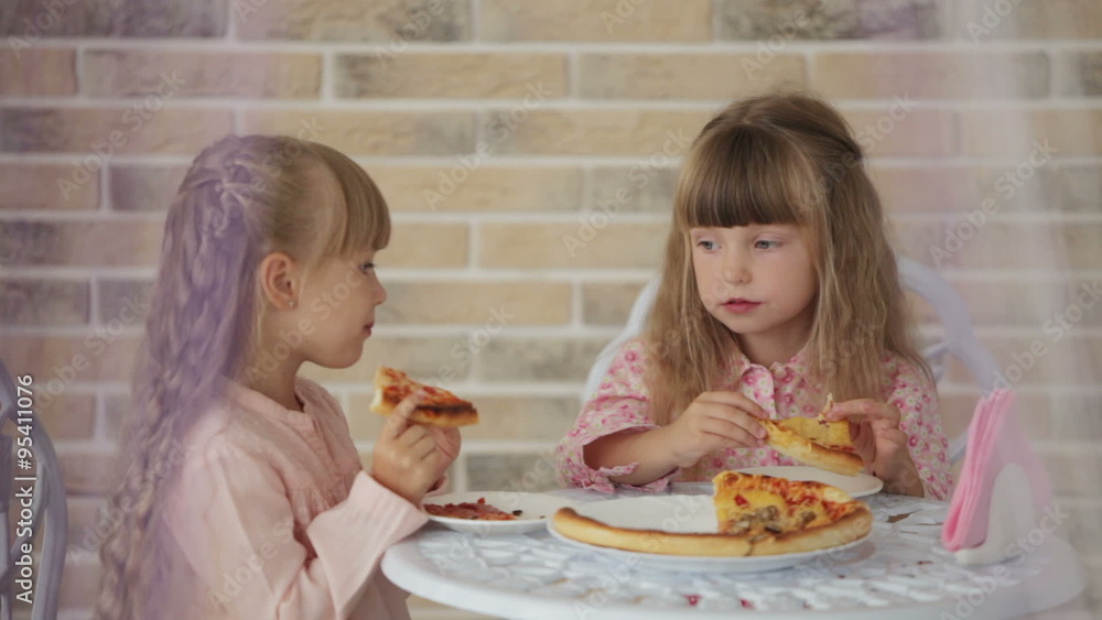 Two cute little girls sitting at table at cafe eating pizza and smiling Two cute little girls sitting at table at cafe eating pizza and smiling