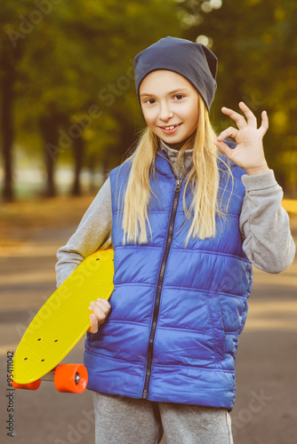 Smiling girl holding color plastic penny board or skateboards outdoor and showing Ok