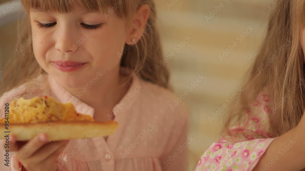 Two funny little girls eating pizza and smiling at camera Two funny little girls eating pizza and smiling at camera