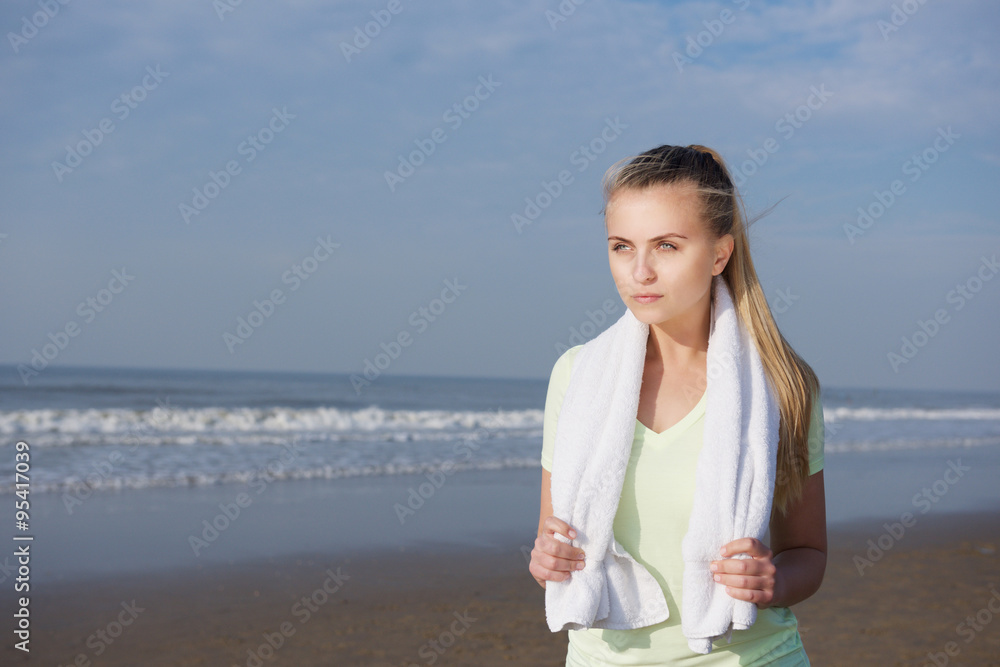 Young fitness woman standing at the beach with towel Young fitness woman standing at the beach with towel
