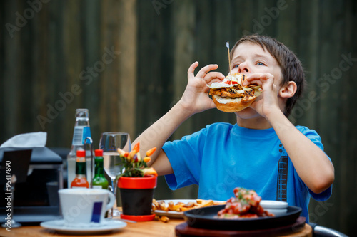 Cute healthy teenager boy eats hamburger and potato