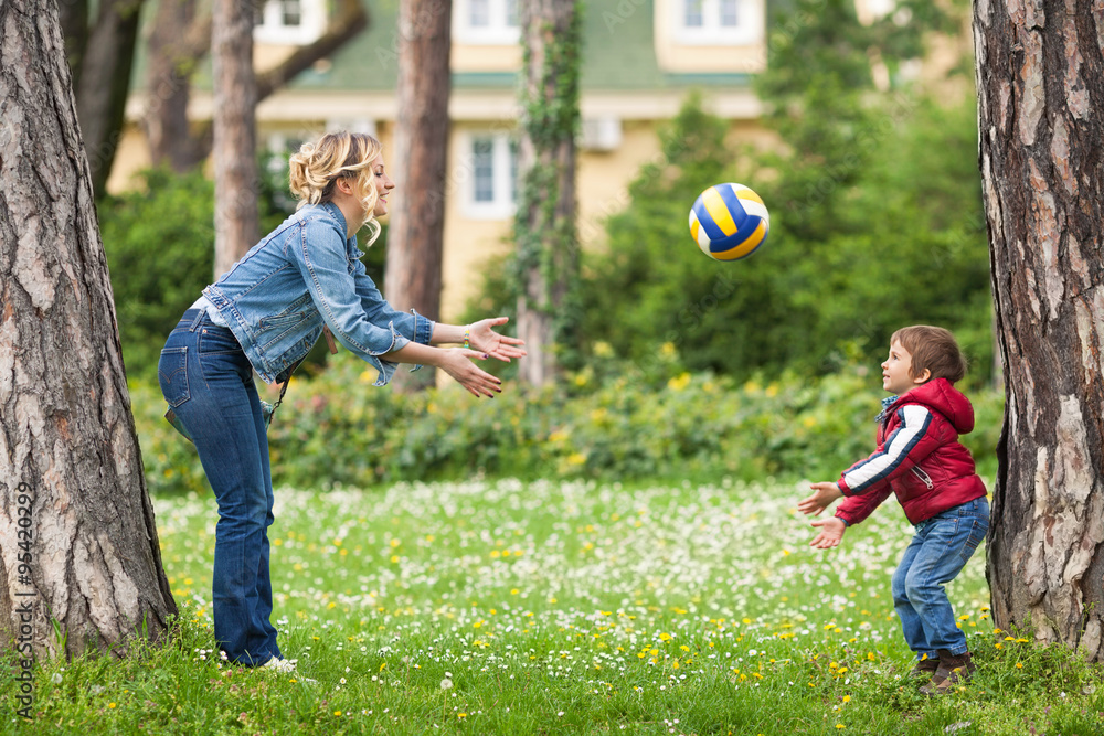 Obraz premium Young mother throwing a ball to her cute little son while playing in a park