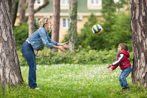 Young mother throwing a ball to her cute little son while playing in a park