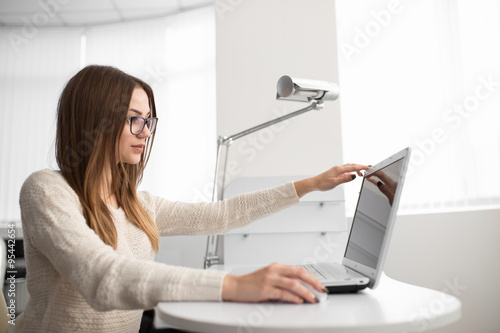 Young woman office worker. She open notebook in light workplace.
