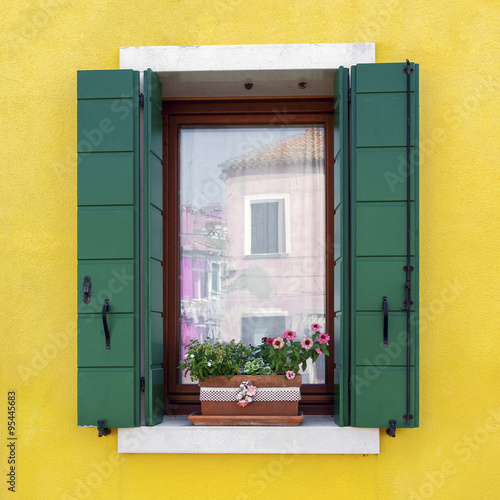 Traditional colorful residential house window with opened shutters and flower pot in venetian island of Burano