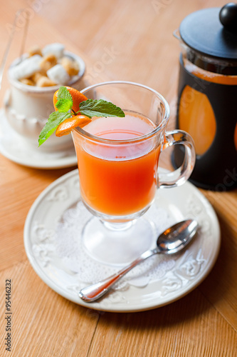 Fruit red tea with orange in glass cup, on wooden table, on bright background
