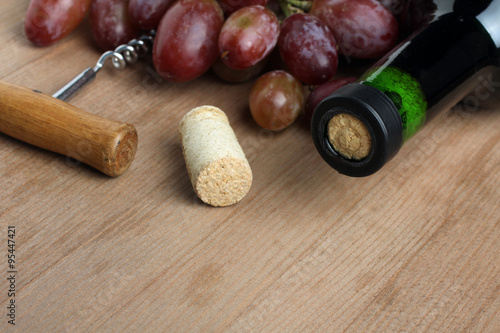 wine bottle and grapes near the corkscrew on wooden background