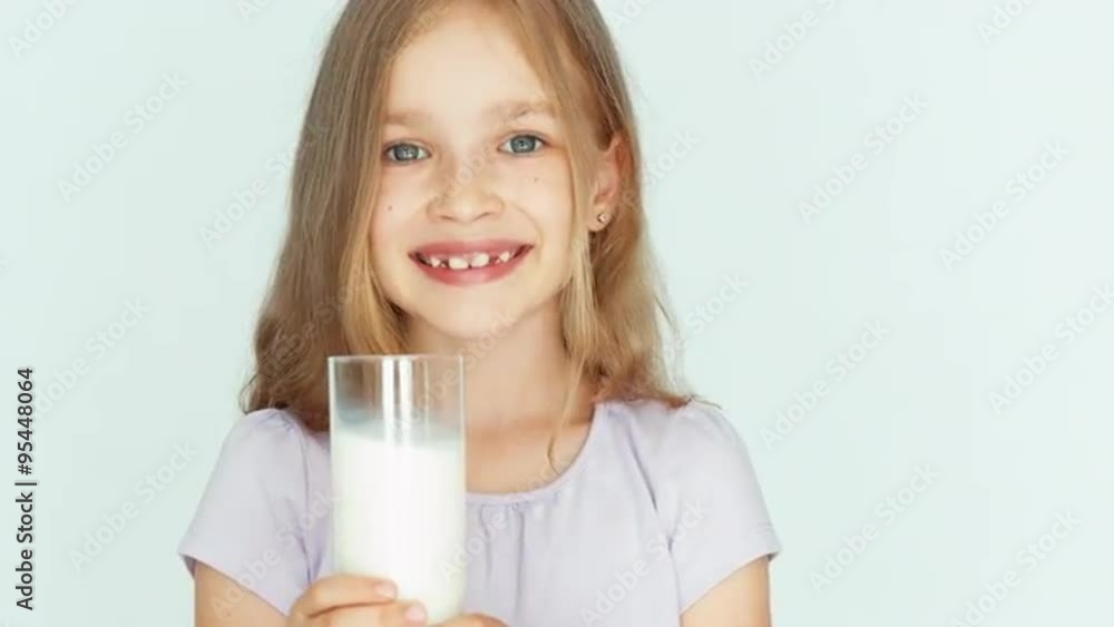 Child drinking milk. Girl showing glass of milk at camera. Girl with beautiful blond hair on a white background. Big eyes. Closeup Child drinking milk. Girl showing glass of milk at camera. Girl with beautiful blond hair on a white background. Big eyes. Closeup