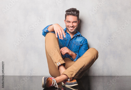 smiling man in denim shirt sitting legs crossed in studio backgr