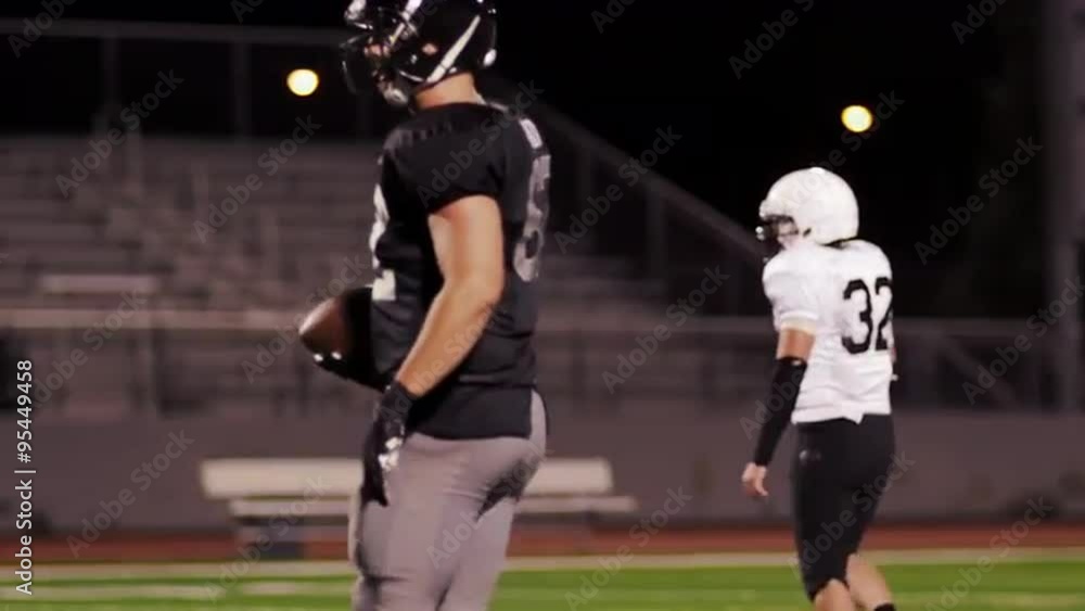 A football player walks up to his teammates on the field at night
A football player walks up to his teammates on the field at night
