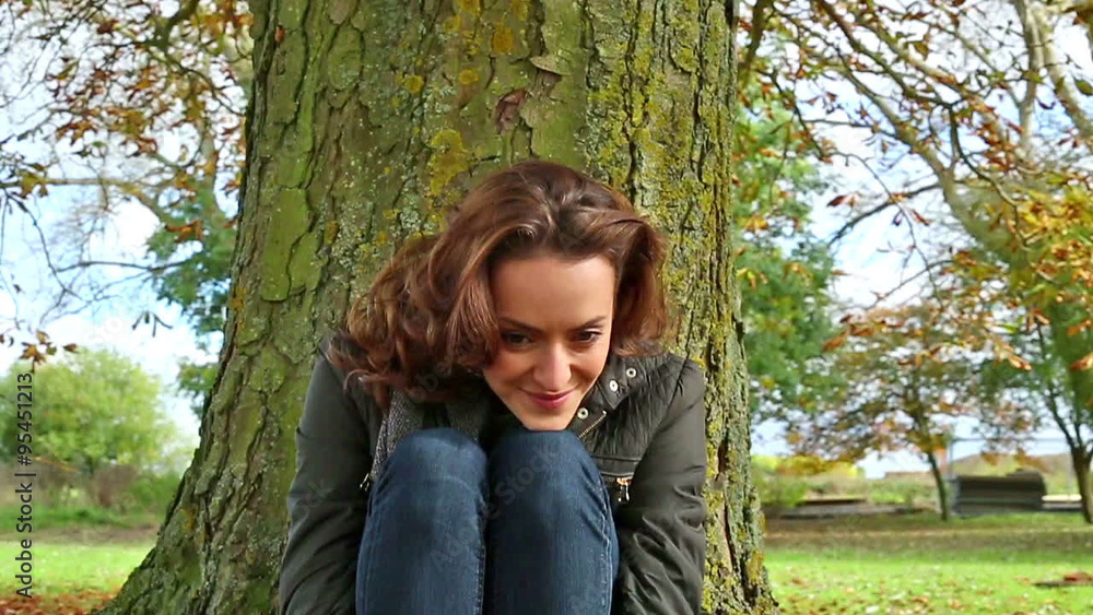 Beautiful young woman leaning against a tree on a bright Autumn day relaxing Beautiful young woman leaning against a tree on a bright Autumn day relaxing