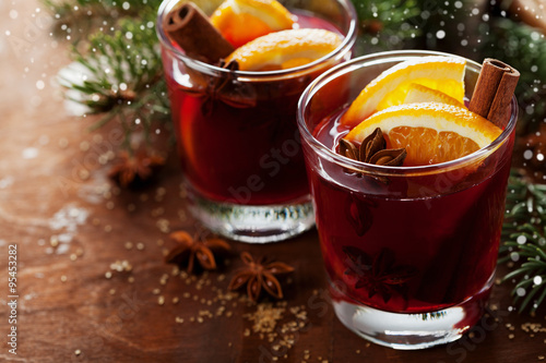 Christmas mulled wine or gluhwein with spices and orange slices on rustic table, traditional drink on winter holiday, magic light, selective focus
