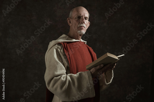Obraz na plátně Official portrait of monk holding book. Studio shot against dark